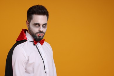 Man in scary vampire costume with fangs on orange background, space for text. Halloween celebration