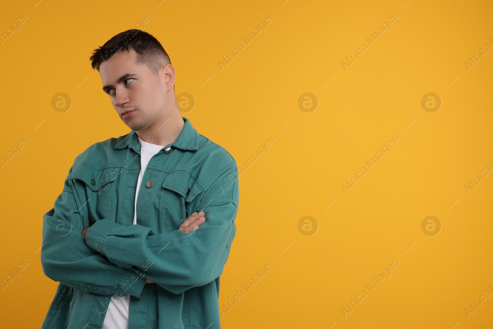 Photo of Resentful man with crossed arms on orange background, space for text