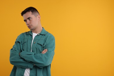 Photo of Resentful man with crossed arms on orange background, space for text