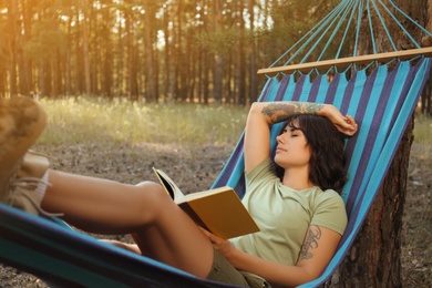 Woman with book resting in comfortable hammock outdoors