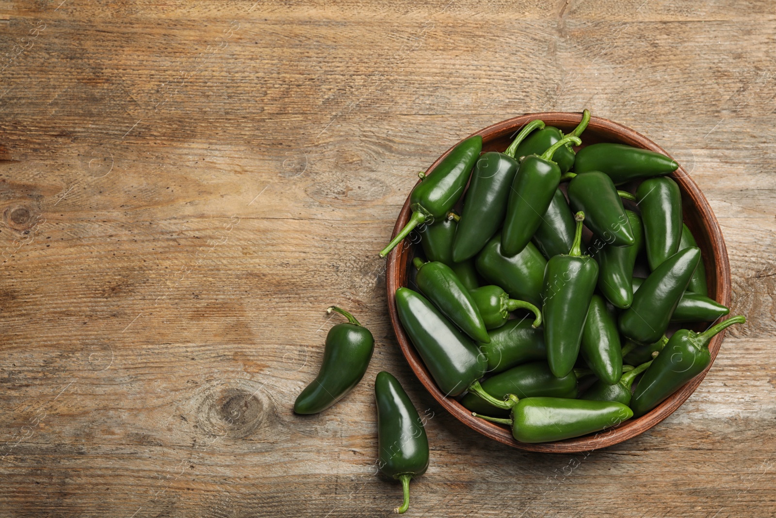 Photo of Bowl with green hot chili peppers on wooden table, flat lay. Space for text