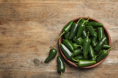 Bowl with green hot chili peppers on wooden table, flat lay. Space for text