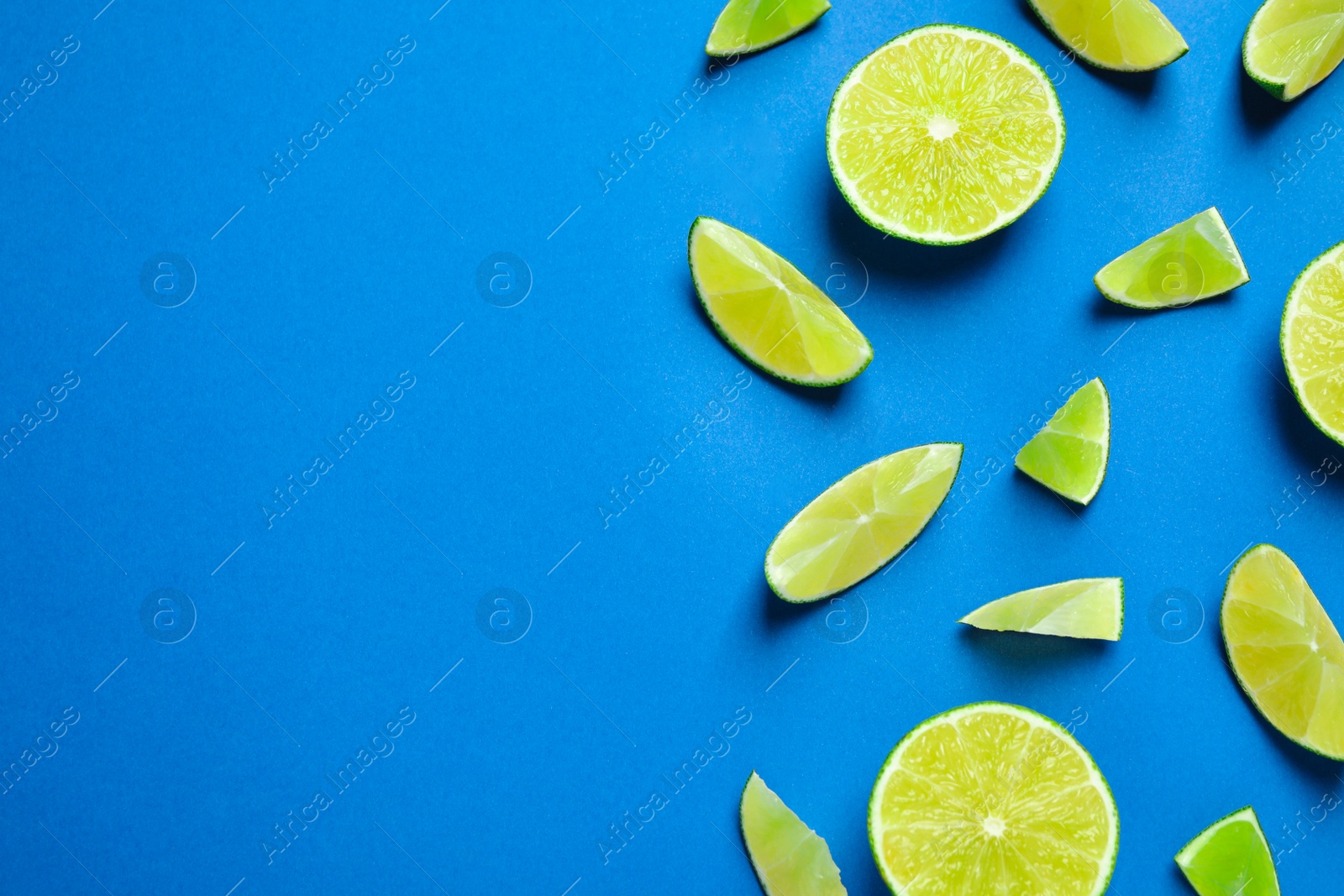 Photo of Juicy fresh lime slices on blue background, flat lay. Space for text