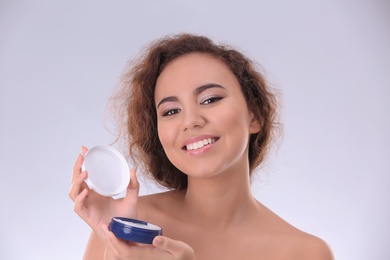 Beautiful young woman with problem skin applying anti acne cream on light background