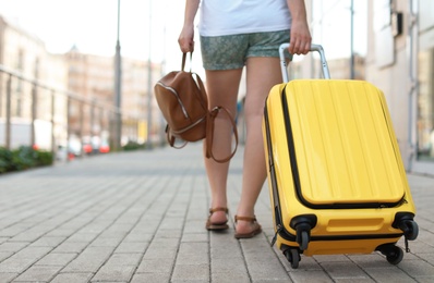 Young woman with yellow carry on suitcase outdoors