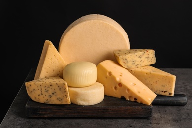 Photo of Wooden board with different sorts of cheese on table against black background