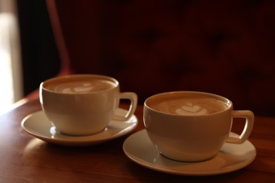 Photo of Cups of aromatic coffee with foam on wooden table in cafe