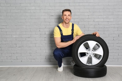 Male mechanic with car tires on brick wall background