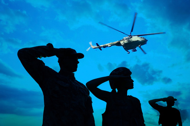 Image of Silhouettes of soldiers in uniform saluting and military helicopter outdoors