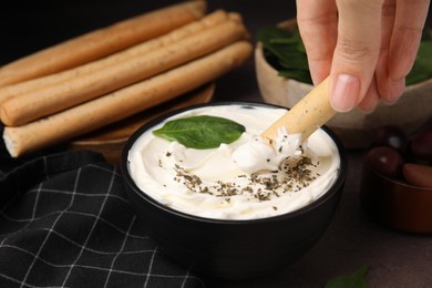 Photo of Woman dipping tasty grissini stick into creamy cheese at table, closeup