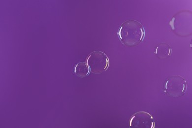 Beautiful transparent soap bubbles on violet background, space for text