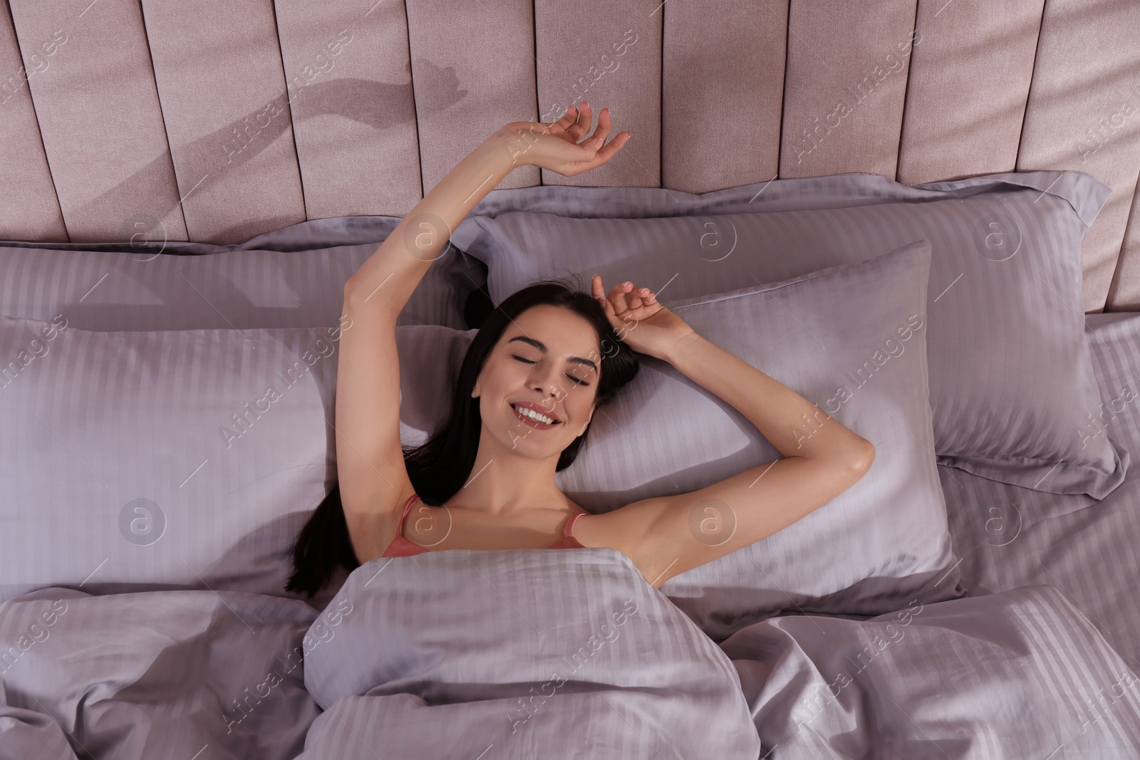 Photo of Woman awakening in comfortable bed with light grey striped linens, above view