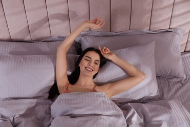 Woman awakening in comfortable bed with light grey striped linens, above view