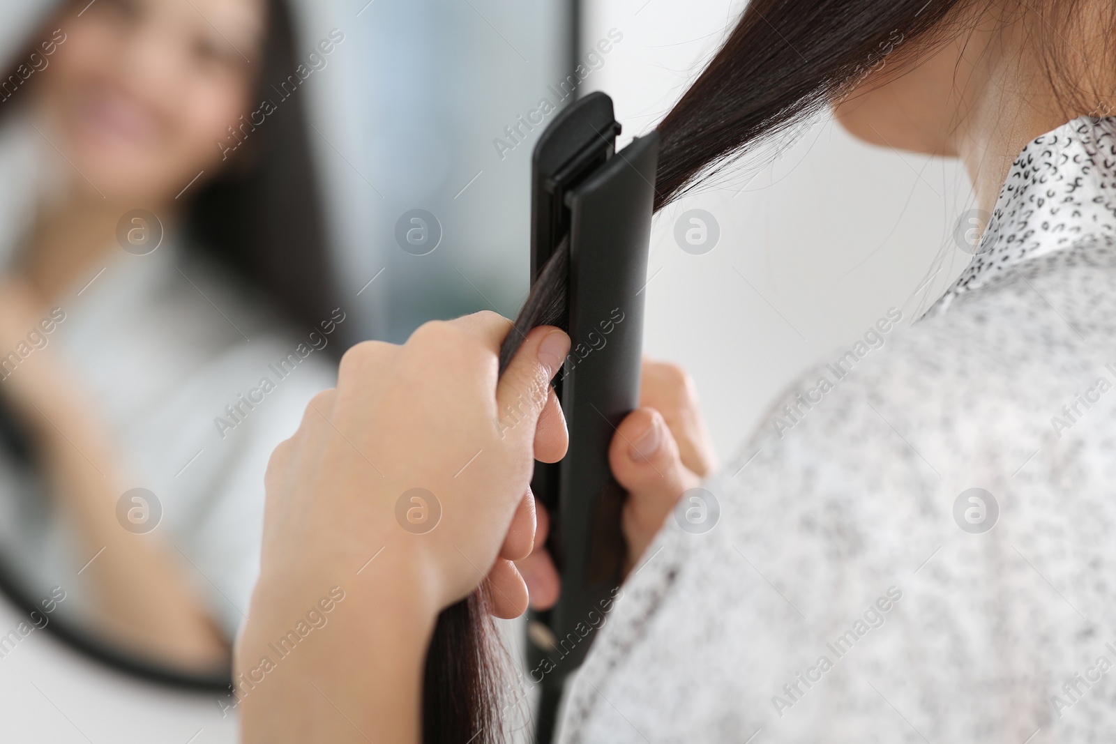 Photo of Woman using hair iron near mirror indoors, closeup. Space for text