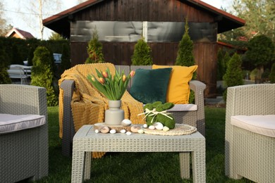 Photo of Terrace with Easter decorations. Bouquet of tulips in vase, bunny figures and decorative eggs on table outdoors