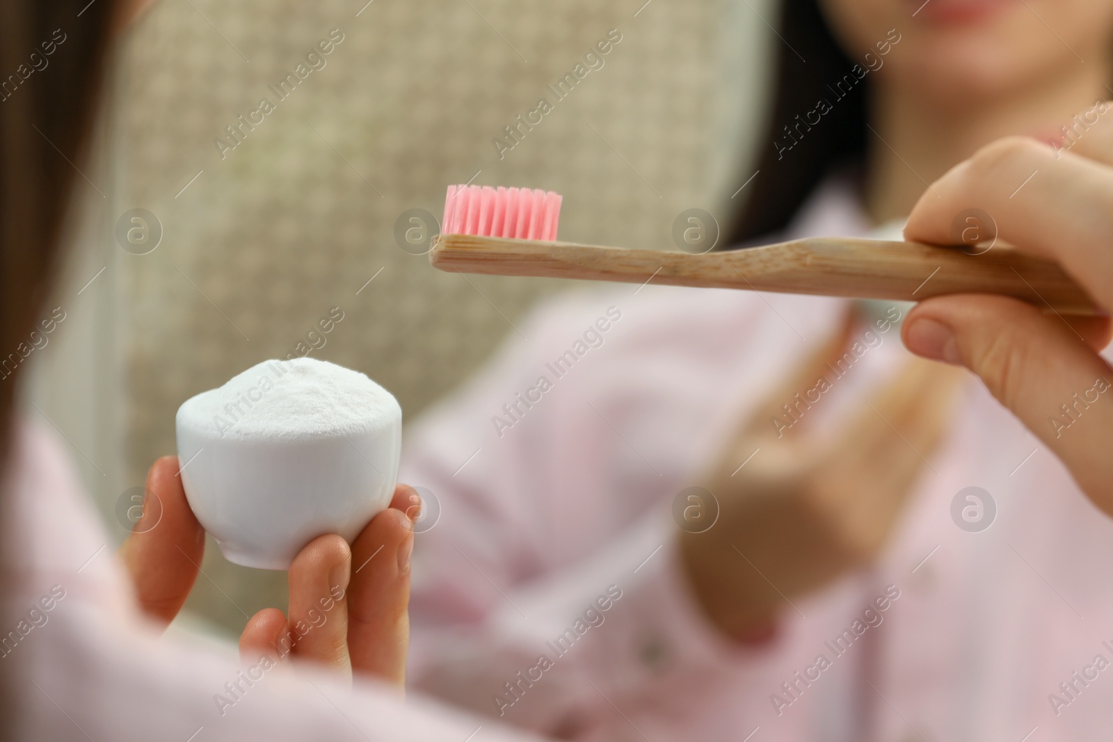 Photo of Young woman with toothbrush and bowl of baking soda near mirror indoors, closeup