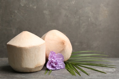 Photo of Young peeled coconuts with palm leaf and beautiful flower on grey table. Space for text