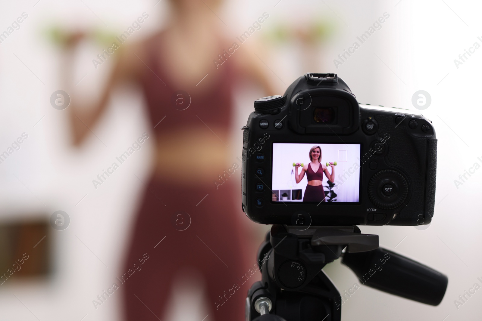 Photo of Smiling sports blogger working out with dumbbells while recording fitness lesson at home, focus on camera. Space for text