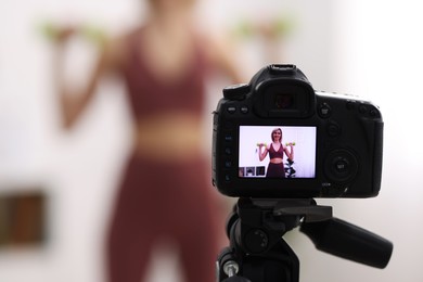 Smiling sports blogger working out with dumbbells while recording fitness lesson at home, focus on camera. Space for text