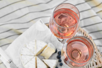 Glasses of delicious rose wine, food and basket on white picnic blanket, closeup