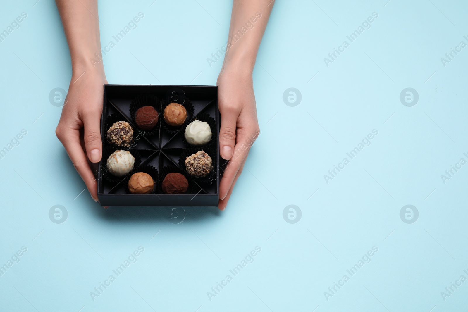 Photo of Woman with box of delicious chocolate candies on light blue background, top view. Space for text