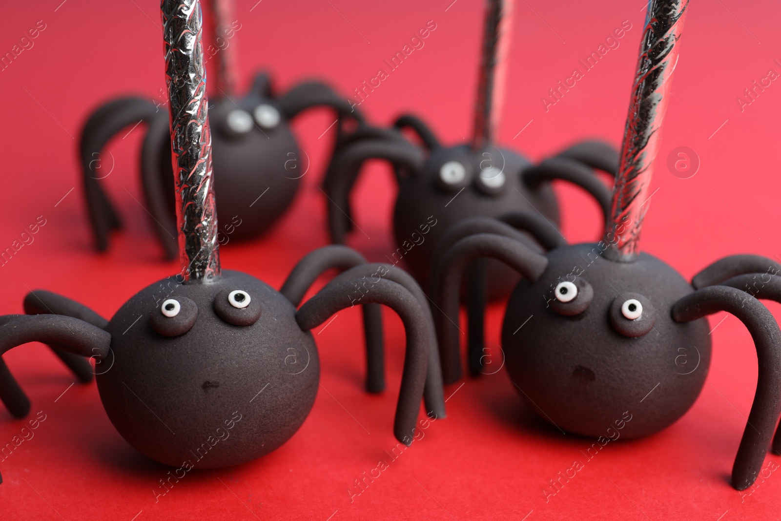 Photo of Delicious spider shaped cake pops on red background, closeup. Halloween treat