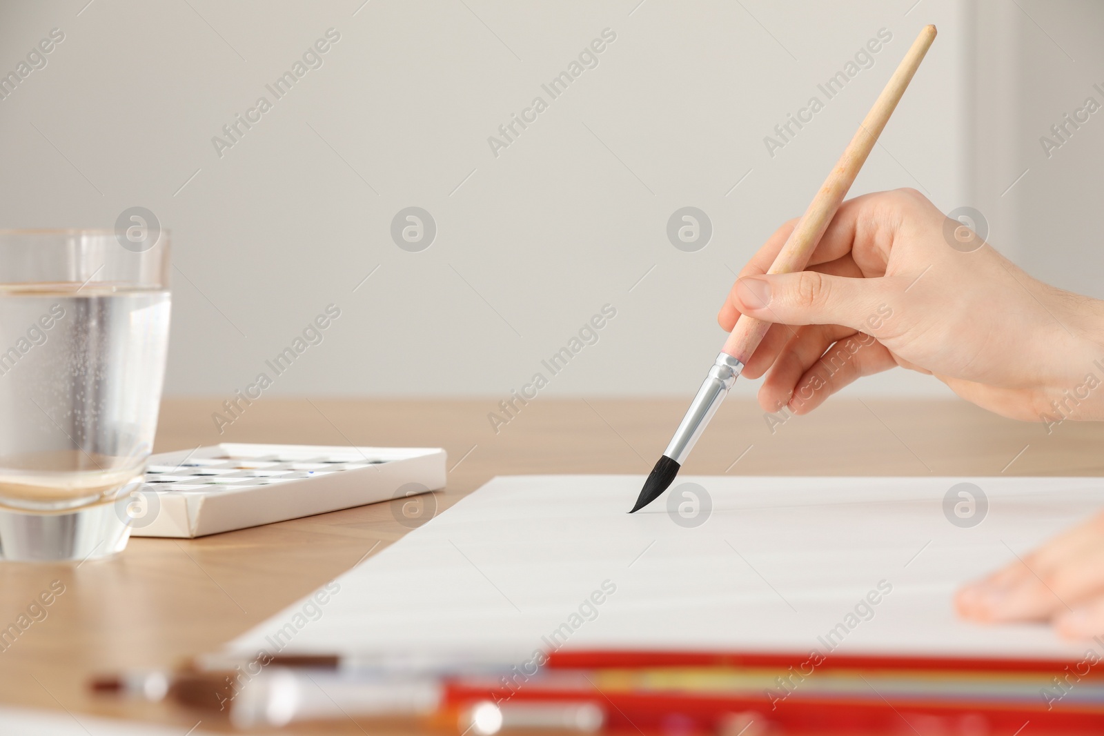 Photo of Woman with brush and paint at wooden table indoors, closeup. Watercolor artwork