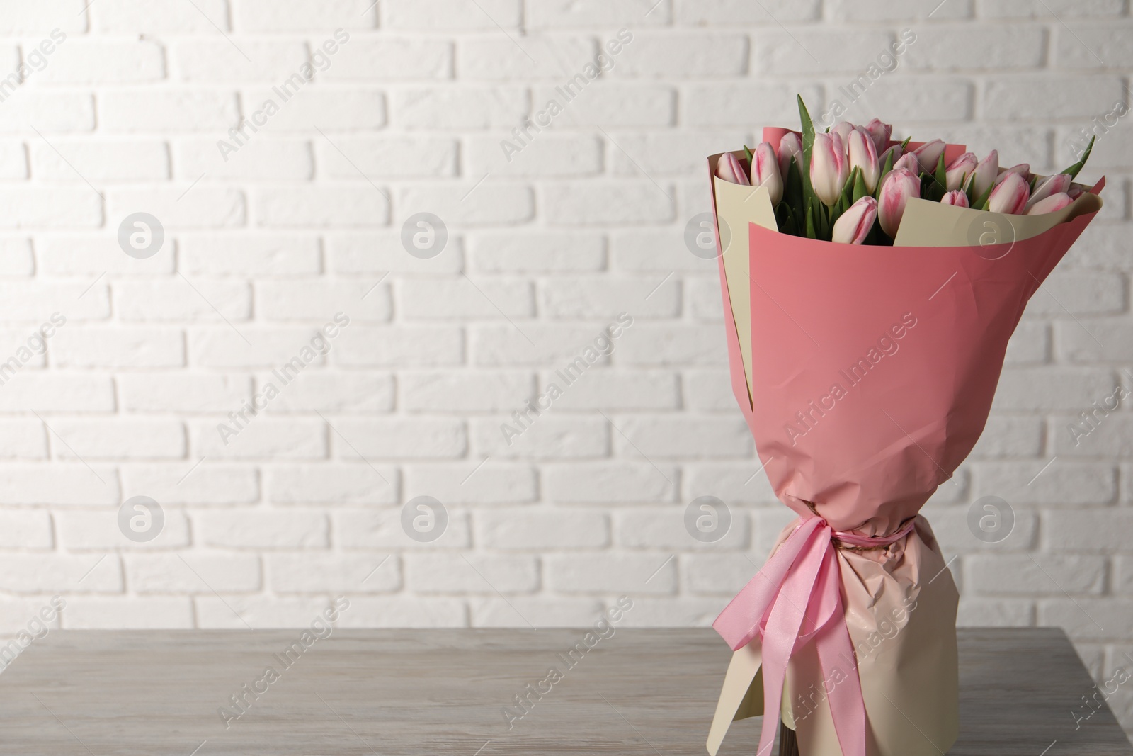 Photo of Beautiful bouquet of fresh pink tulips on light wooden table. Space for text