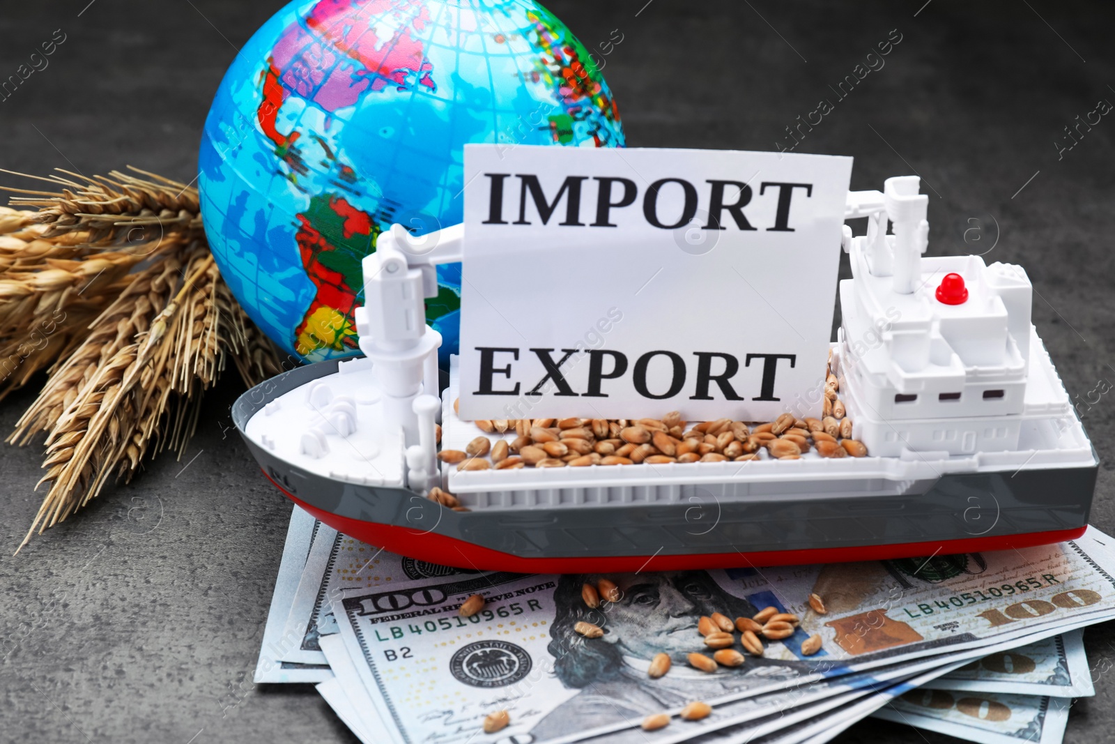 Photo of Card with words Import and Export. globe, ears of wheat and toy vessel cargo on grey table