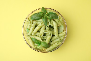 Photo of Delicious pasta with pesto sauce and basil on yellow background, top view