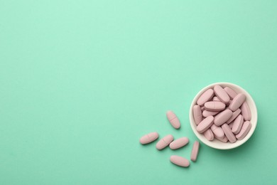 Photo of Pink vitamin capsules and bowl on turquoise background, top view. Space for text