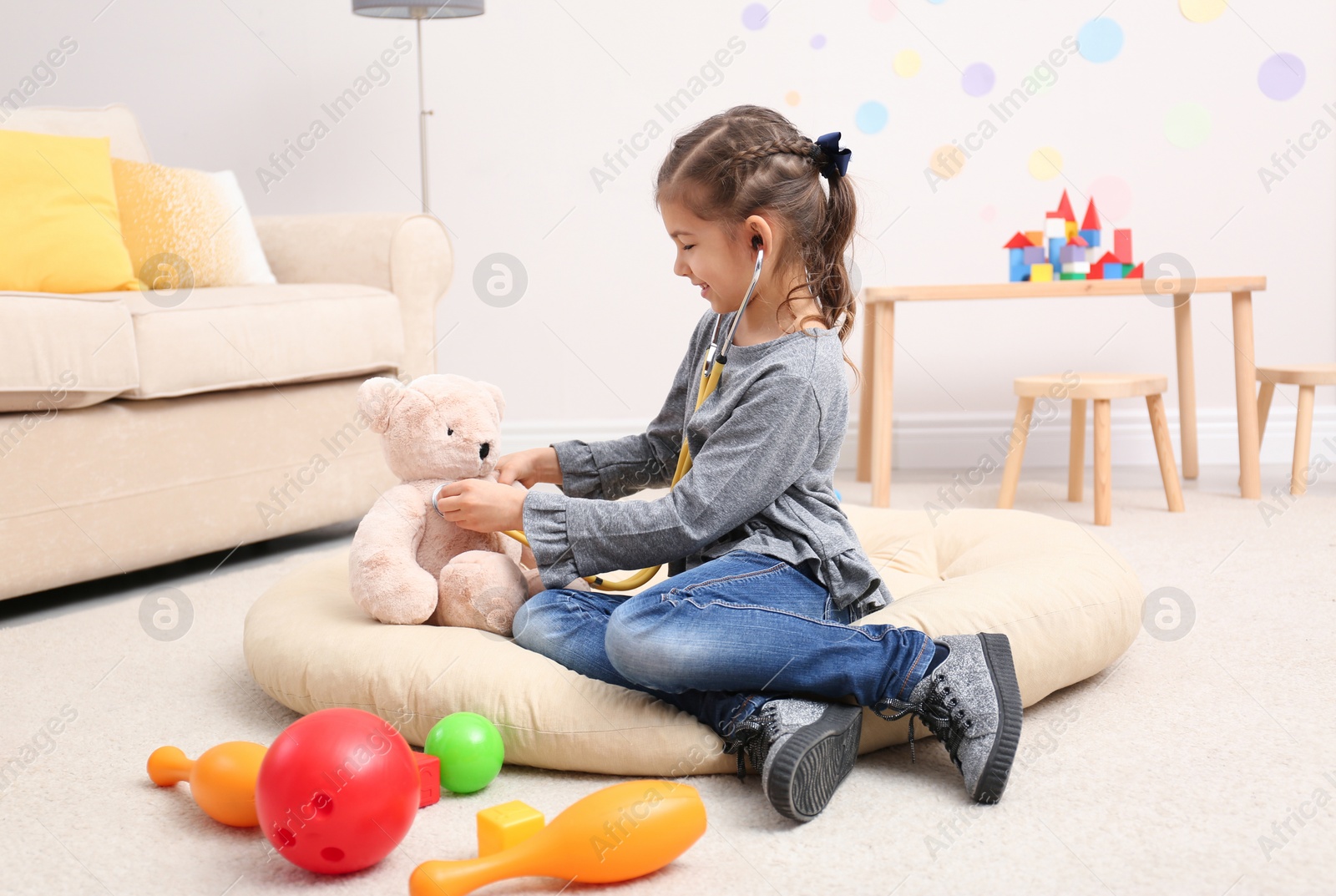 Photo of Cute child playing doctor with stuffed toy on floor in hospital