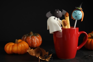 Photo of Different cake pops in cup decorated as monsters on black table. Halloween treat