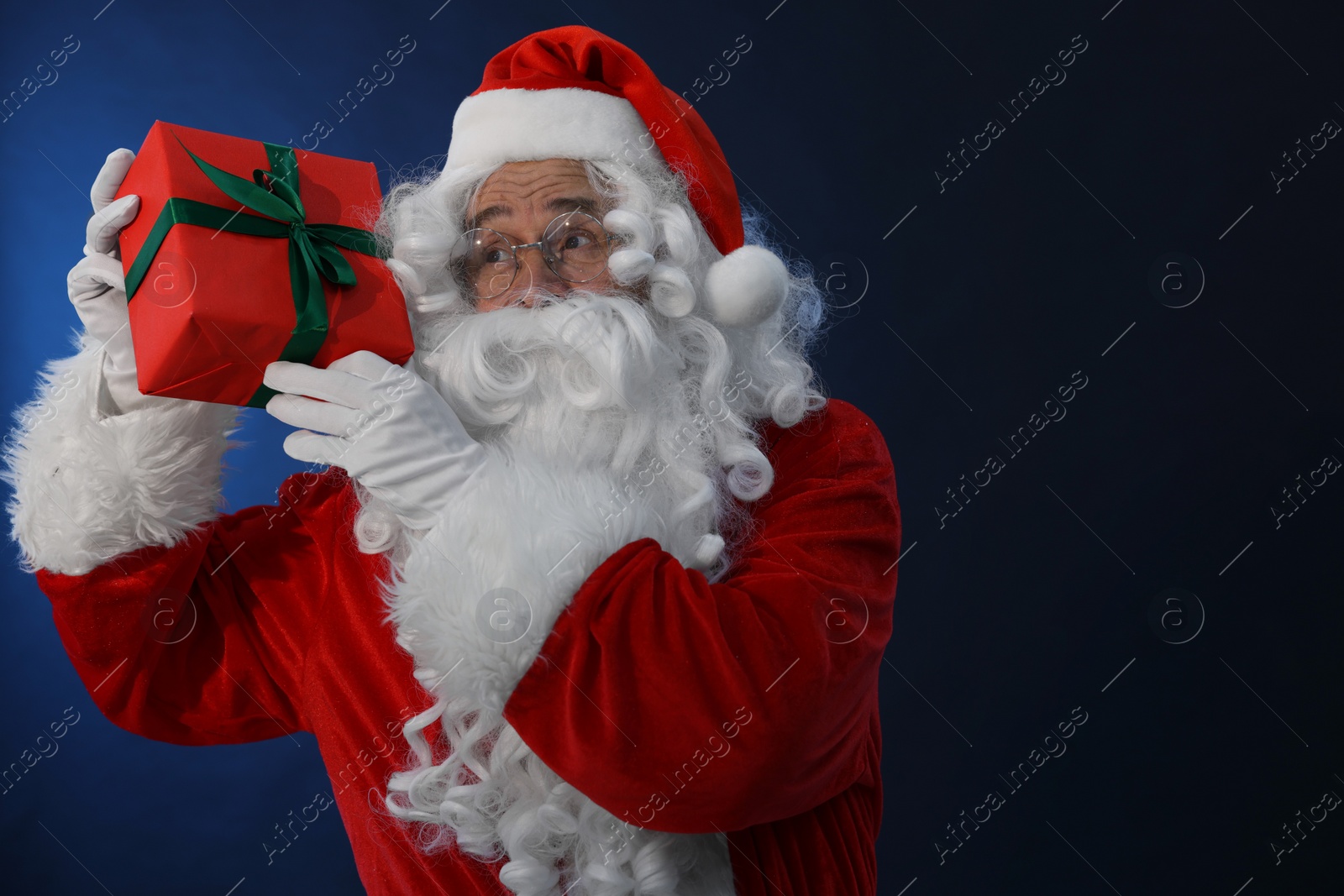 Photo of Santa Claus with Christmas gift on dark blue background. Space for text