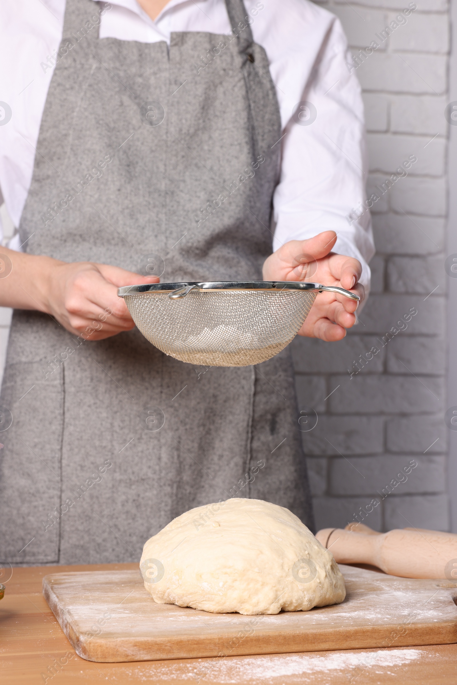 Photo of Woman sprinkling flour over dough at table near white brick wall, closeup