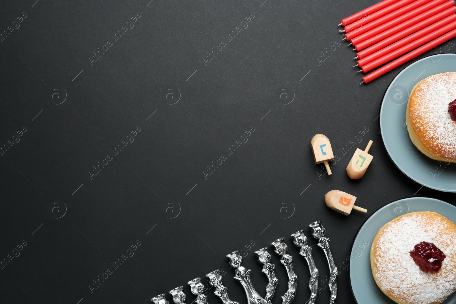 Photo of Hanukkah traditional menorah, candles, doughnuts, dreidels with letters He, Pe, Nun, Gimel on black background, flat lay. Space for text