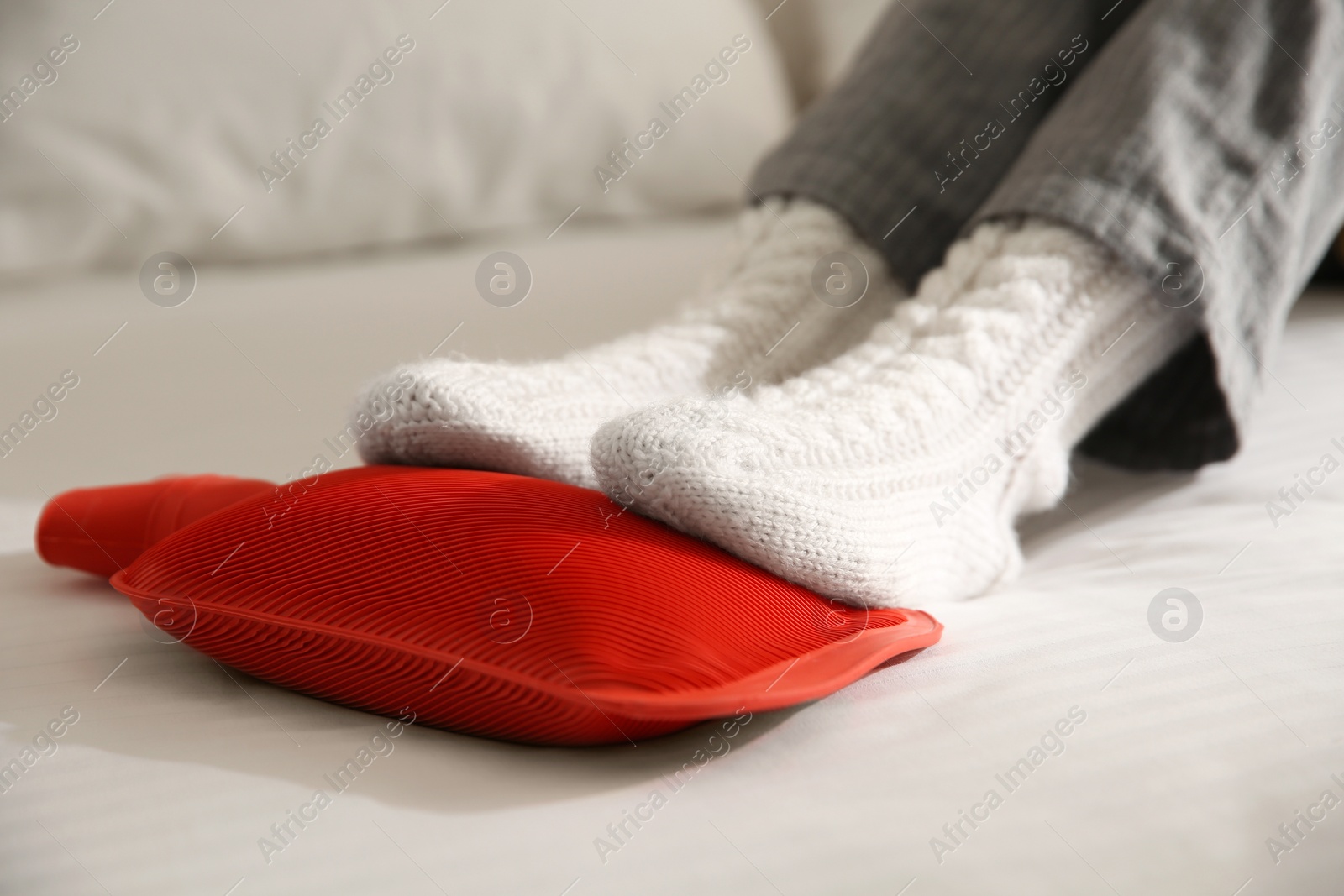 Photo of Person warming feet with hot water bottle on bed, closeup