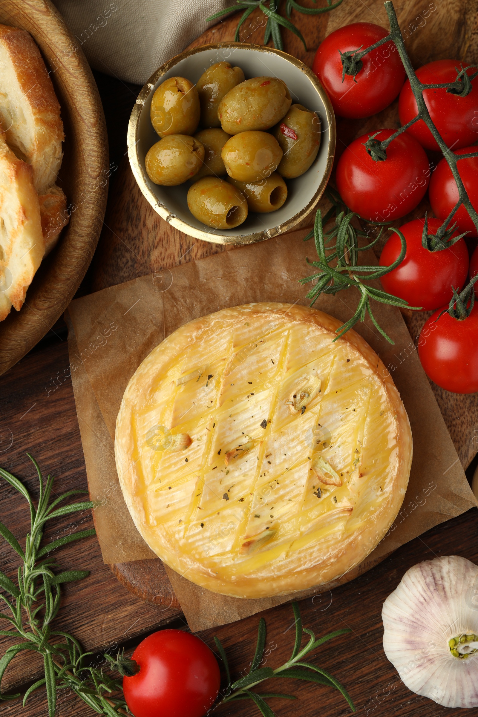 Photo of Tasty baked brie cheese served on wooden table, flat lay