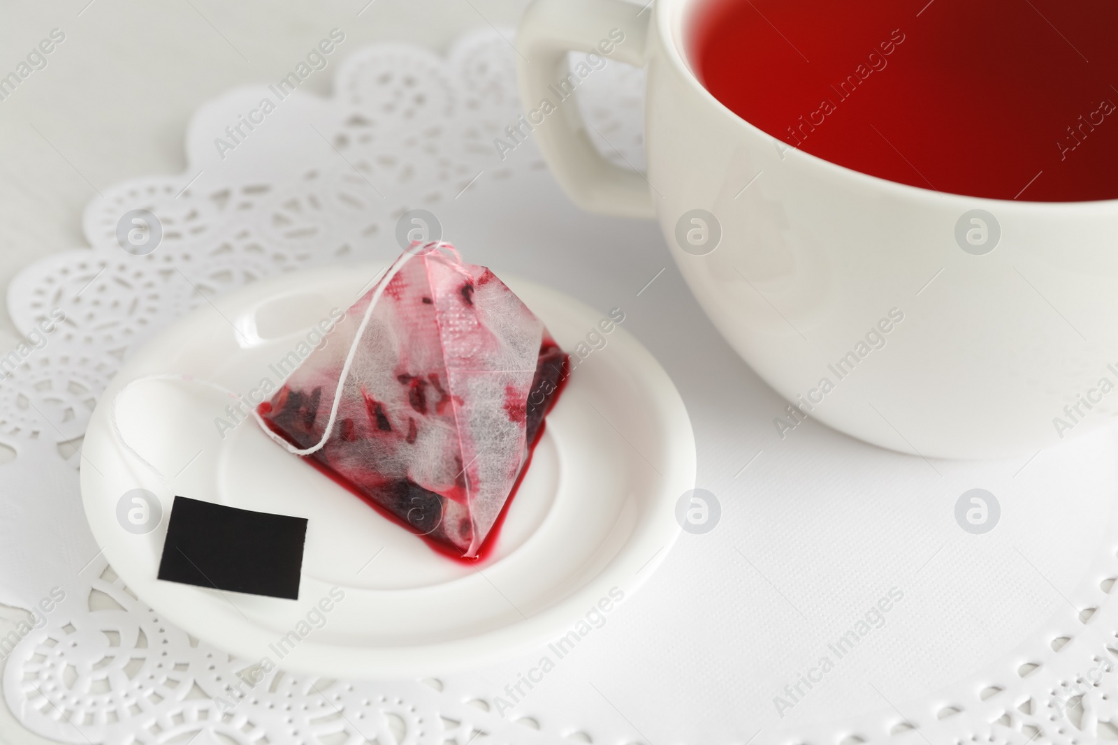 Photo of Saucer with used tea bag near cup on table