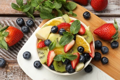 Photo of Tasty fruit salad in bowl and ingredients on wooden table, flat lay