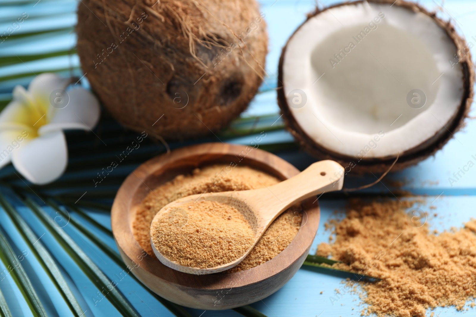 Photo of Coconut sugar, palm leaves, fruits and flower on light blue wooden table, closeup