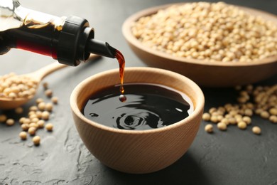 Photo of Pouring tasty soy sauce from bottle into bowl on black table, closeup