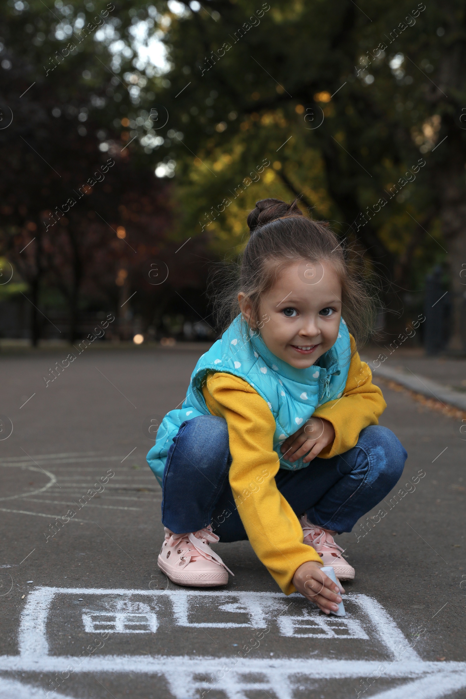 Photo of Child drawing house with chalk on asphalt