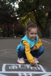 Child drawing house with chalk on asphalt