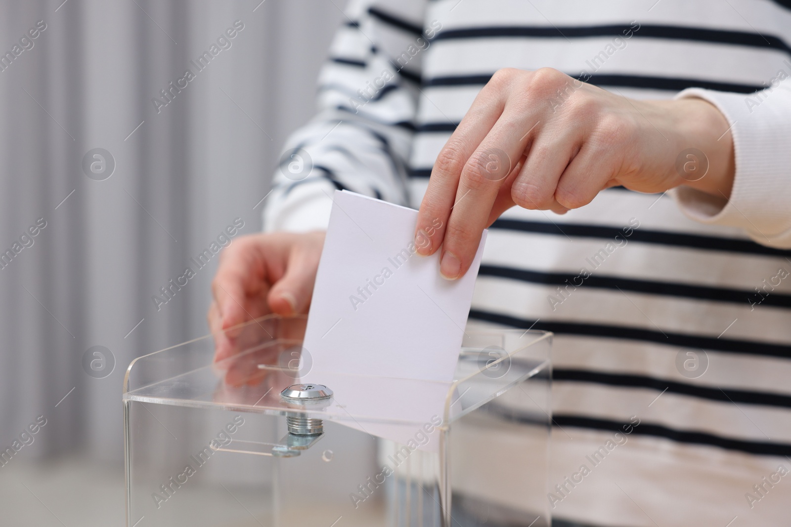 Photo of Woman putting her vote into ballot box on blurred background, closeup