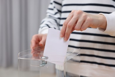 Photo of Woman putting her vote into ballot box on blurred background, closeup