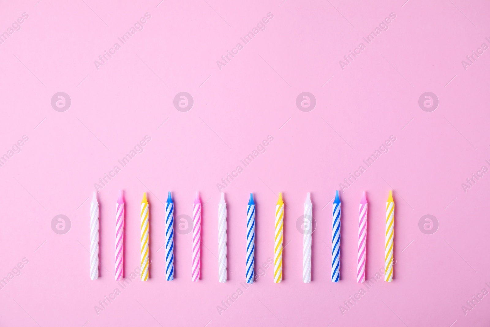 Photo of Colorful striped birthday candles on pink background, flat lay. Space for text