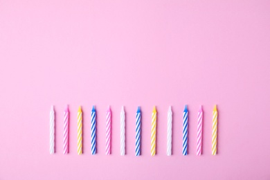 Colorful striped birthday candles on pink background, flat lay. Space for text