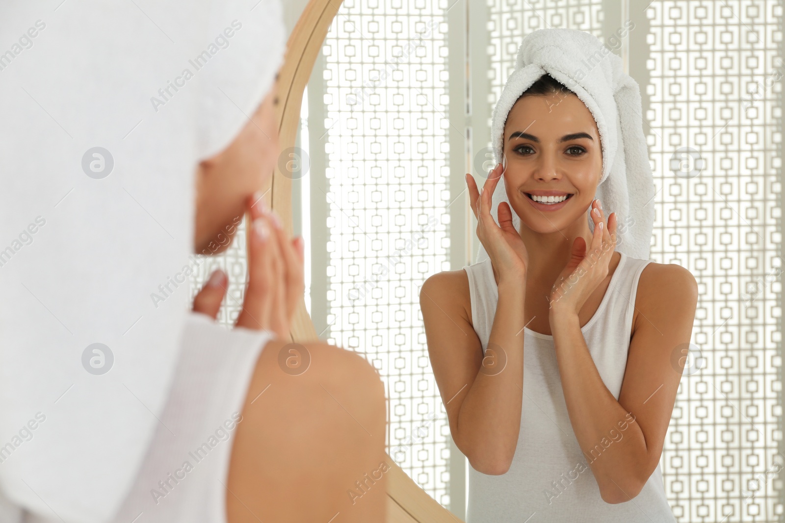 Photo of Happy young woman with clean skin looking at mirror in bathroom
