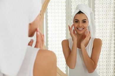 Happy young woman with clean skin looking at mirror in bathroom